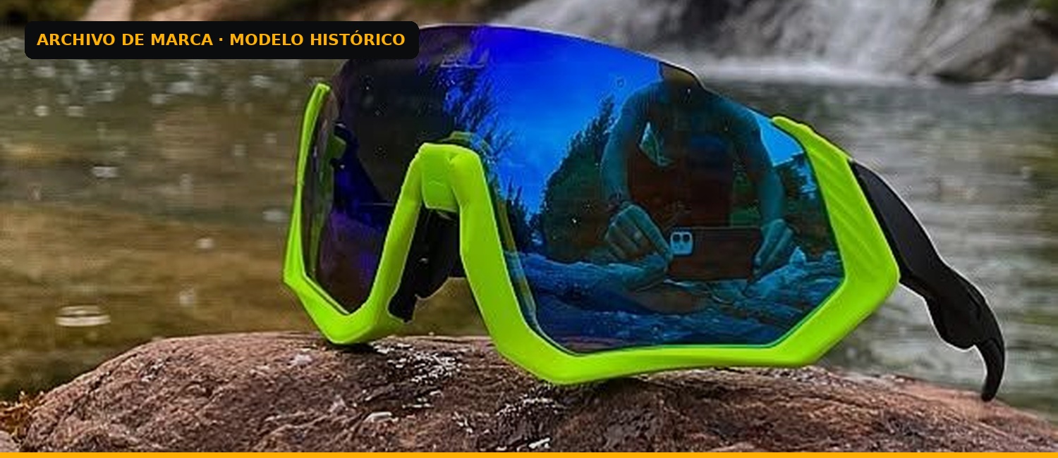 Gafas ISGLOW de montura verde y lente azul junto a un río. Modelo histórico.